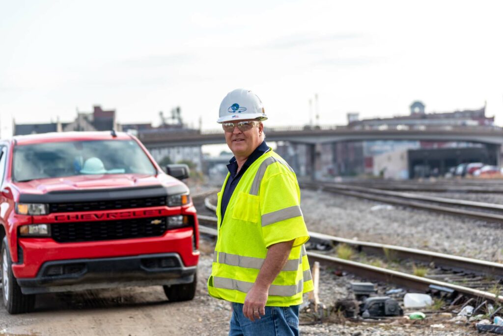 A construction worker standing next to railroad tracks and a red truck